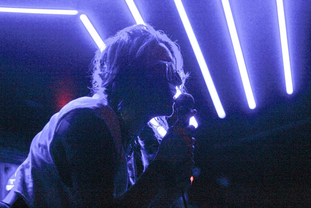 A backlit photo of a person holding a microphone and singing, the phoro is very blue and purple
