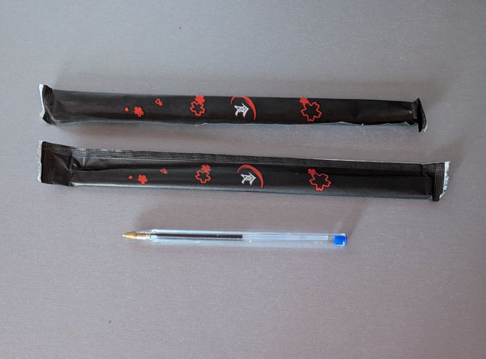 Vista cenital de dos juegos de palillos para comer sushi y un bolígrafo Pérez Reverte (Bic cristal) de color azul. 