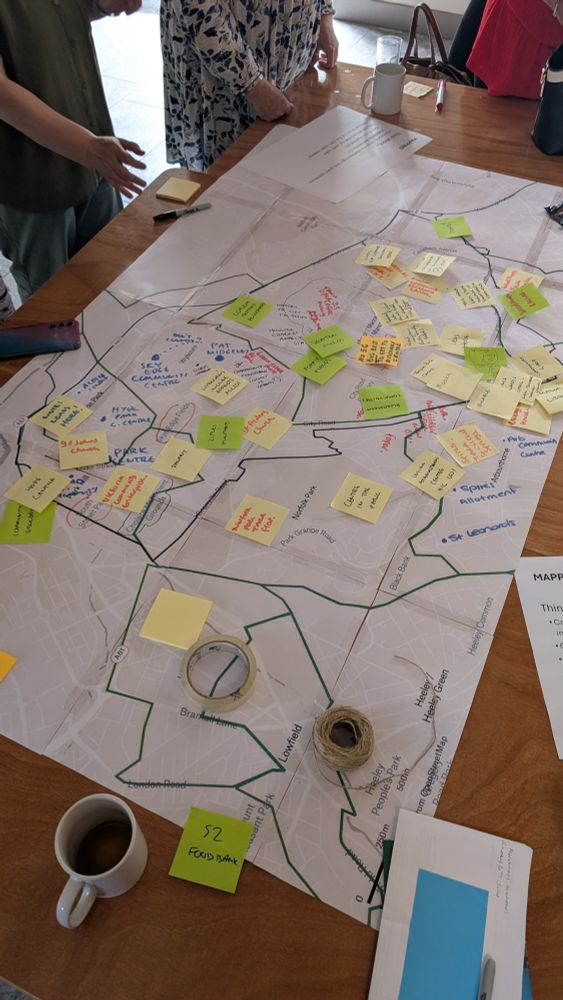 A paper map of the neighbourhoods in and around Manor Castle ward covered in post it notes highlighting positive things in the area. People are stood around the edges.