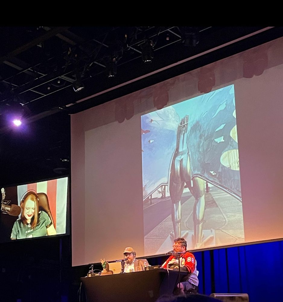 Photo of the Well There’s Your Problem Philadelphia live show with a slide of the Point Pleasant Mothman statue’s dump truck ass on screen behind the hosts.
