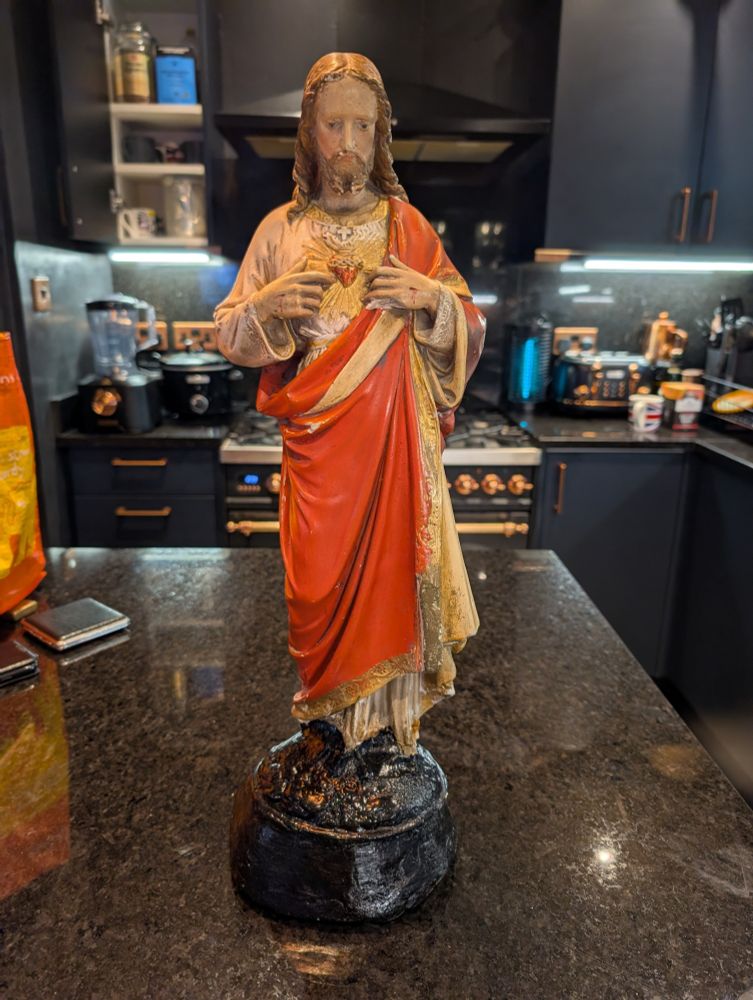 2ft statue of Jesus with sacred heart on a black kitchen work surface with navy kitchen units behind it.