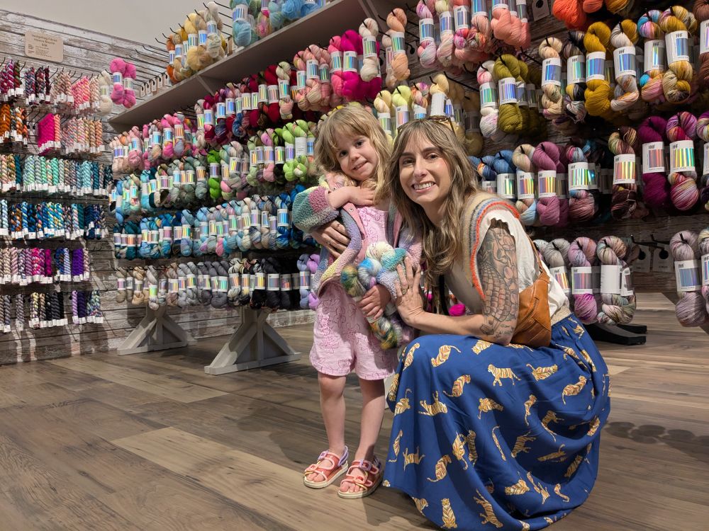 Mom and daughter smiling in front of a rack of hedgehog fibers yarn skeins.