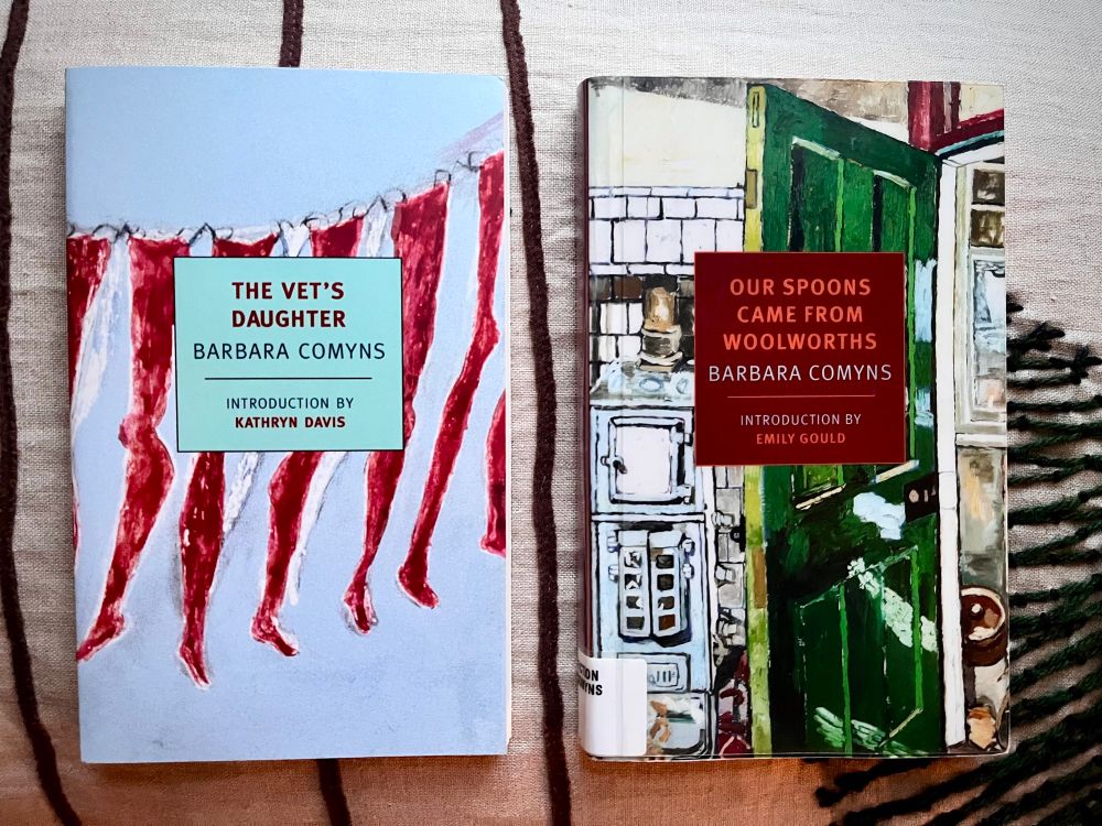 Two books with title cover facing out resting on top a pillow side by side. The left is The Vet’s Daughter and the right Our Spoons Came From Woolworths both written by Barbara Comyns.