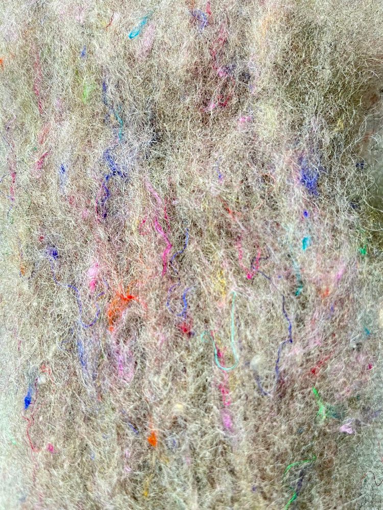 A close up of the unspun fiber from the Touski Melly Knits mega batt. The fiber has a grey base with flecks of multi colored silk.