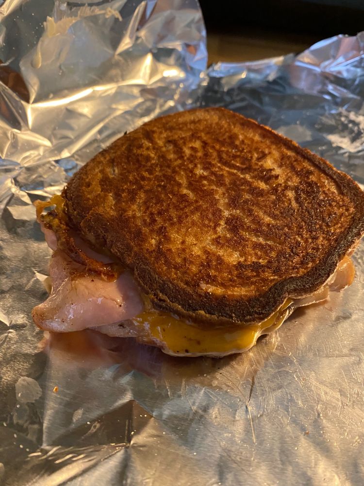 a grilled ham and cheese with a deep golden brown crust on a wrap of tin foil