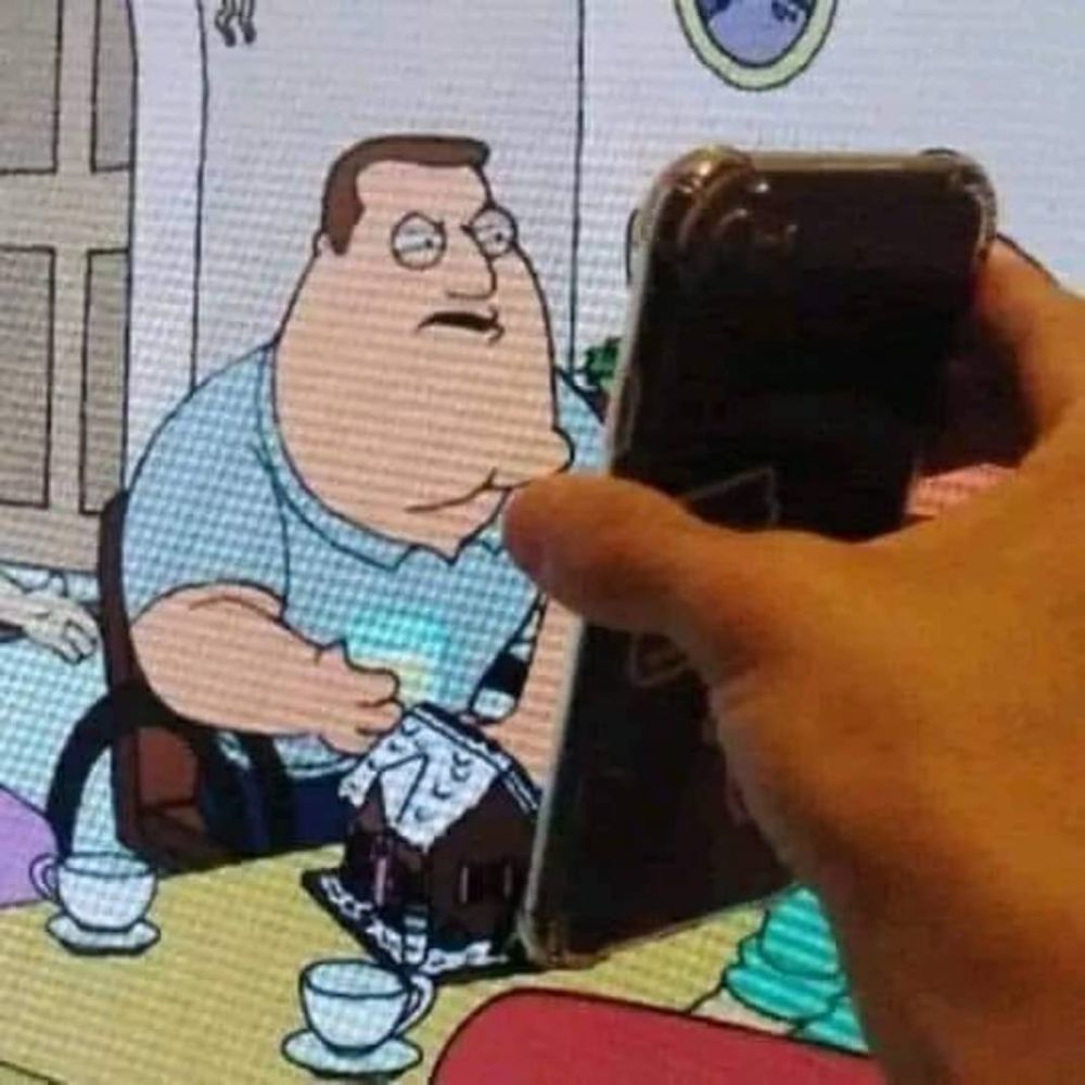 A picture of Joe Swanson, from Family Guy, on a TV. He's leaning forward in his wheelchair with his eyes squinted like he's focusing, with an angry, disgusted look on his face. The person who took the picture of the TV with Joe on it is holding a phone up to the TV. The picture is framed to make it look like Joe is reading/looking at something on the phone, and is upset over what he sees on it