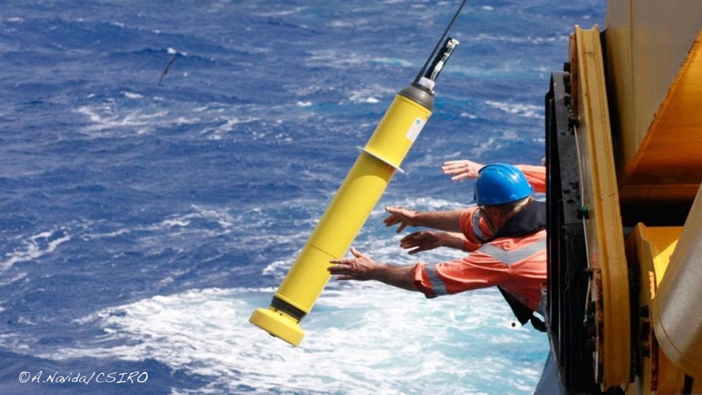 Two crew members with extended arms deploy an Argo Float from a ship.