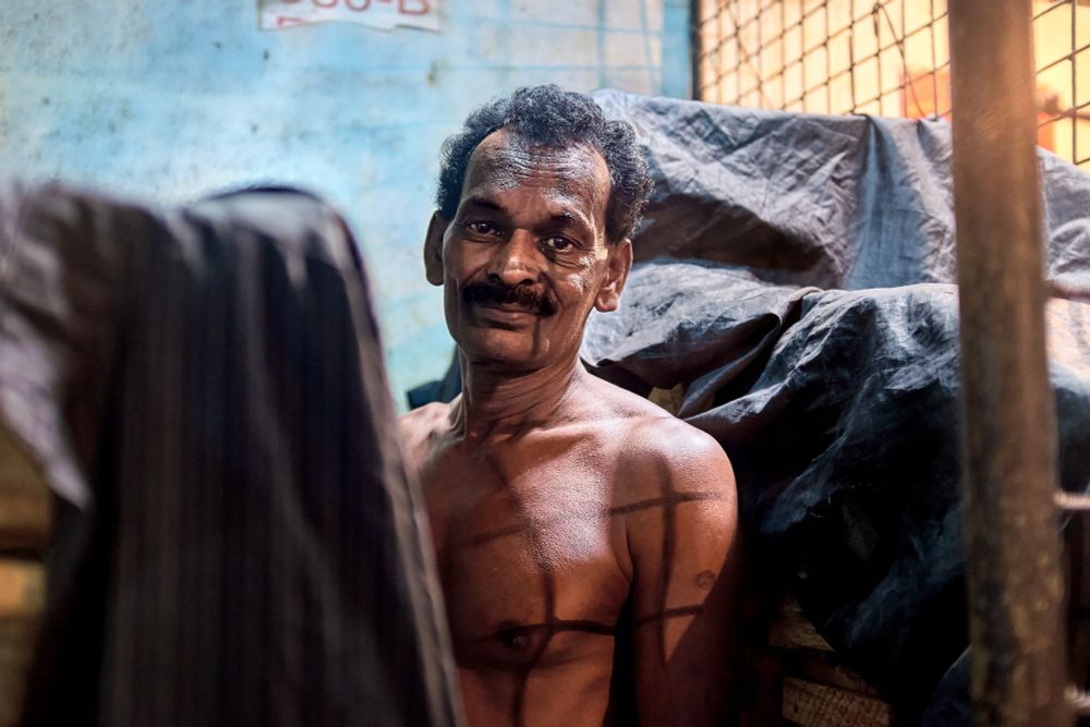A Sri Lankan market worker working in a caged section is crisscrossed from the light above. 