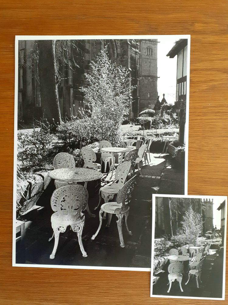 Two times the same image. Both darkroom prints, one 5x7, the other 12x16.
It is of outside, white painted chairs and tables at a café, with a back-lit shrub behind. There is a church in shadow as further background.