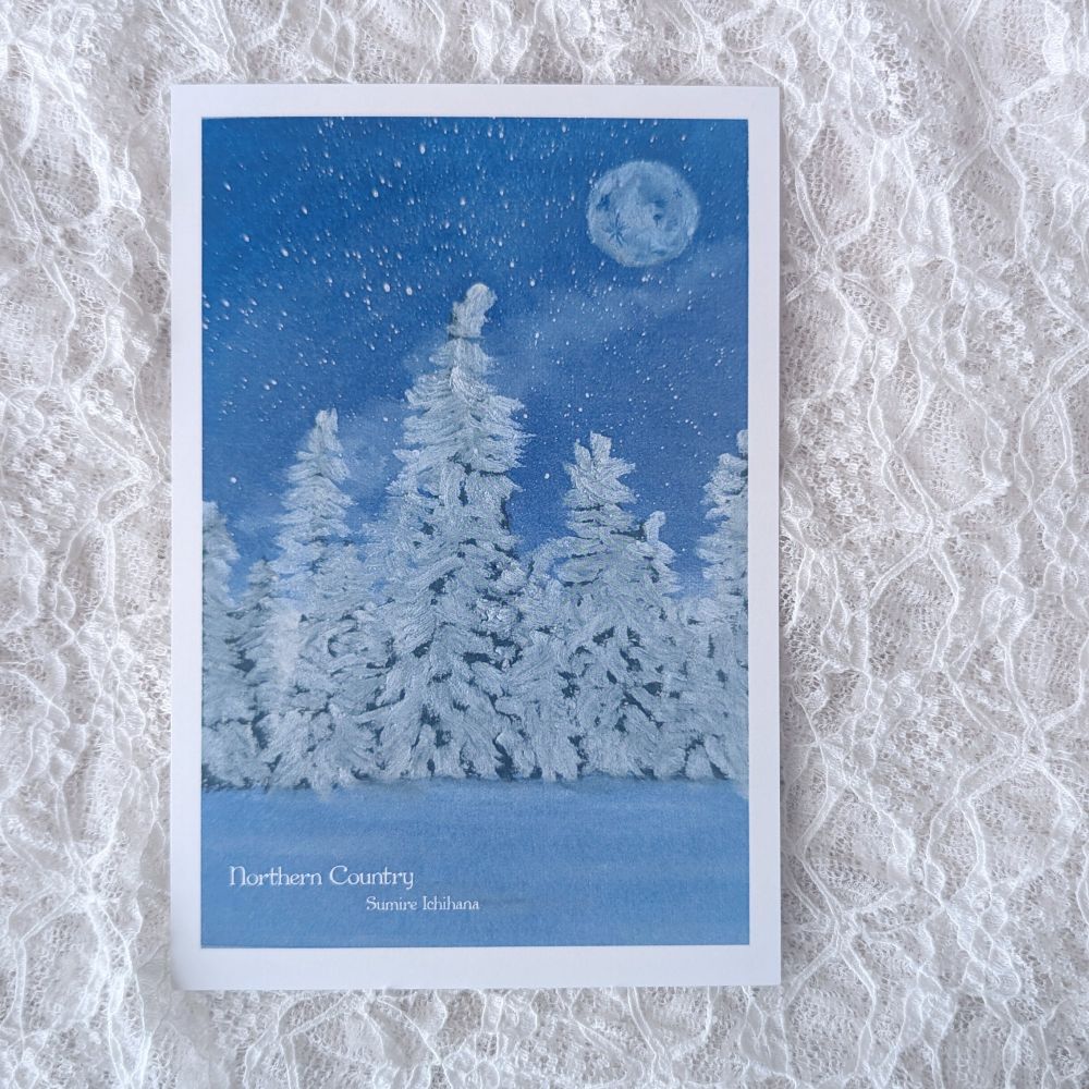 白いレースの布の上に置かれたポストカード。
白い雪が積もった木々が並び、夜空には星と満月、星雲が描かれた幻想的な風景。
魔法使いの約束の北の国の夜をイメージしたオイルパステル画。
下部に《northern country》《SumireIchihana》などの文字が見える。