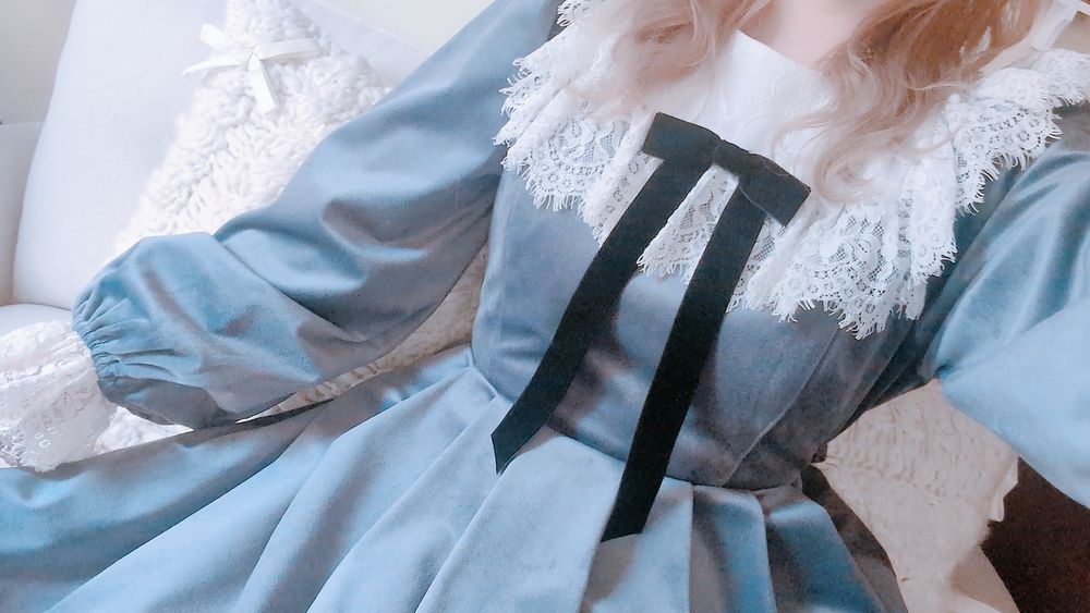 淡いブルーグレーのベロアワンピースを着た人物の首から下の写真。襟と袖には白いレースの装飾があり、胸元には垂れの長いベロアの黒リボンブローチがついている