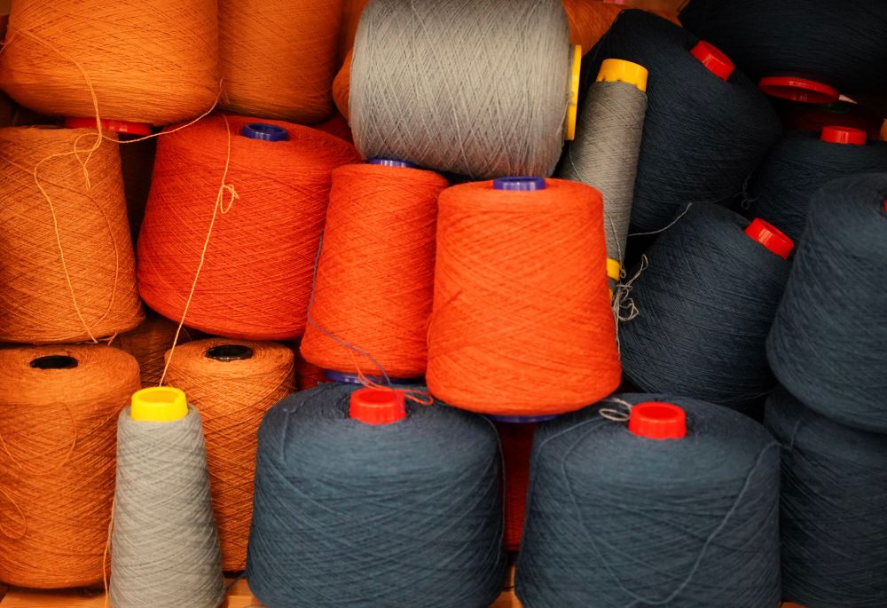 Bobbins of yard at a wool mill. Bright orange left and middle. Some taupe top middle and bottom left. Dark grey on the right and centre.