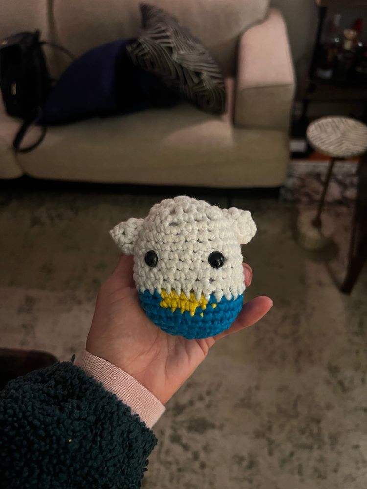 photo of Janie holding a half finished crocheted Hello Kitty Wooble with a blue and yellow outfit on  