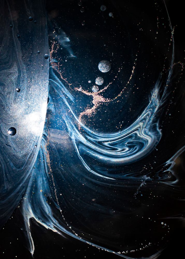 Dark image with half circle that looks like a moon and white spirals coming off the edge that looks like a black hole (but it just household oils in a jar)