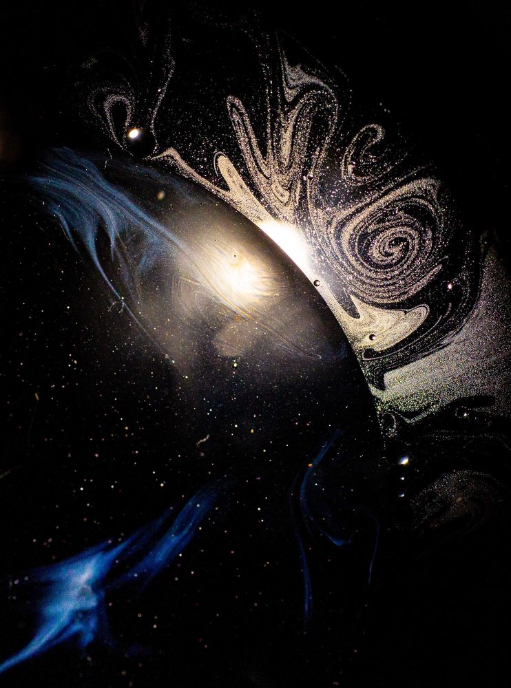 Dark image with half circle and white spirals coming off the edge that looks like a black hole (but it just household oils in a jar)