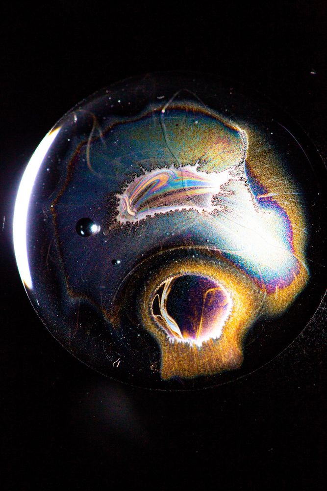 Dark image with half circle and white spirals coming off the edge that looks like a black hole (but it just household oils in a jar)