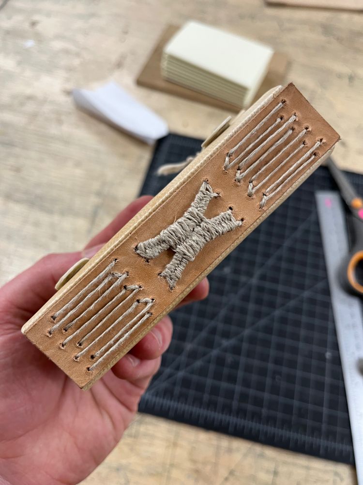 the spine of a medieval-style book with three sections of long stitching, with the center section gathered and cinched together in a weave 