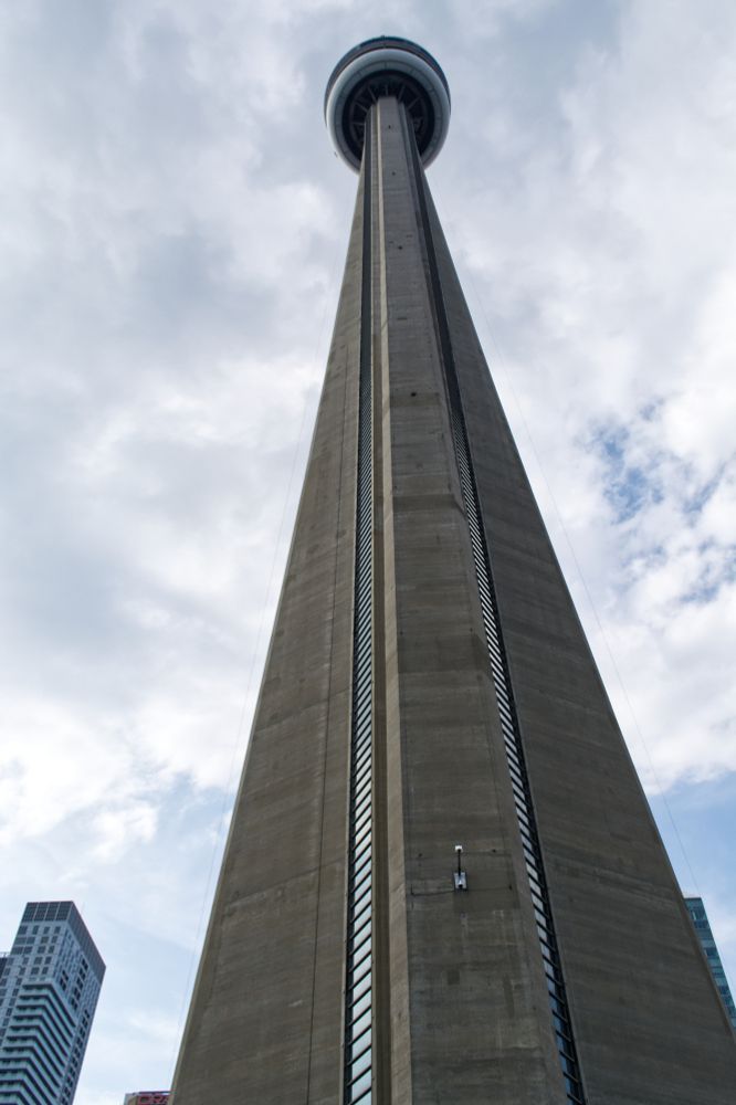 Looking up from the base of the CN tower in Toronto.  The sky is mostly cloudy, with some blue coming through towards the lower part of the photograph. 
