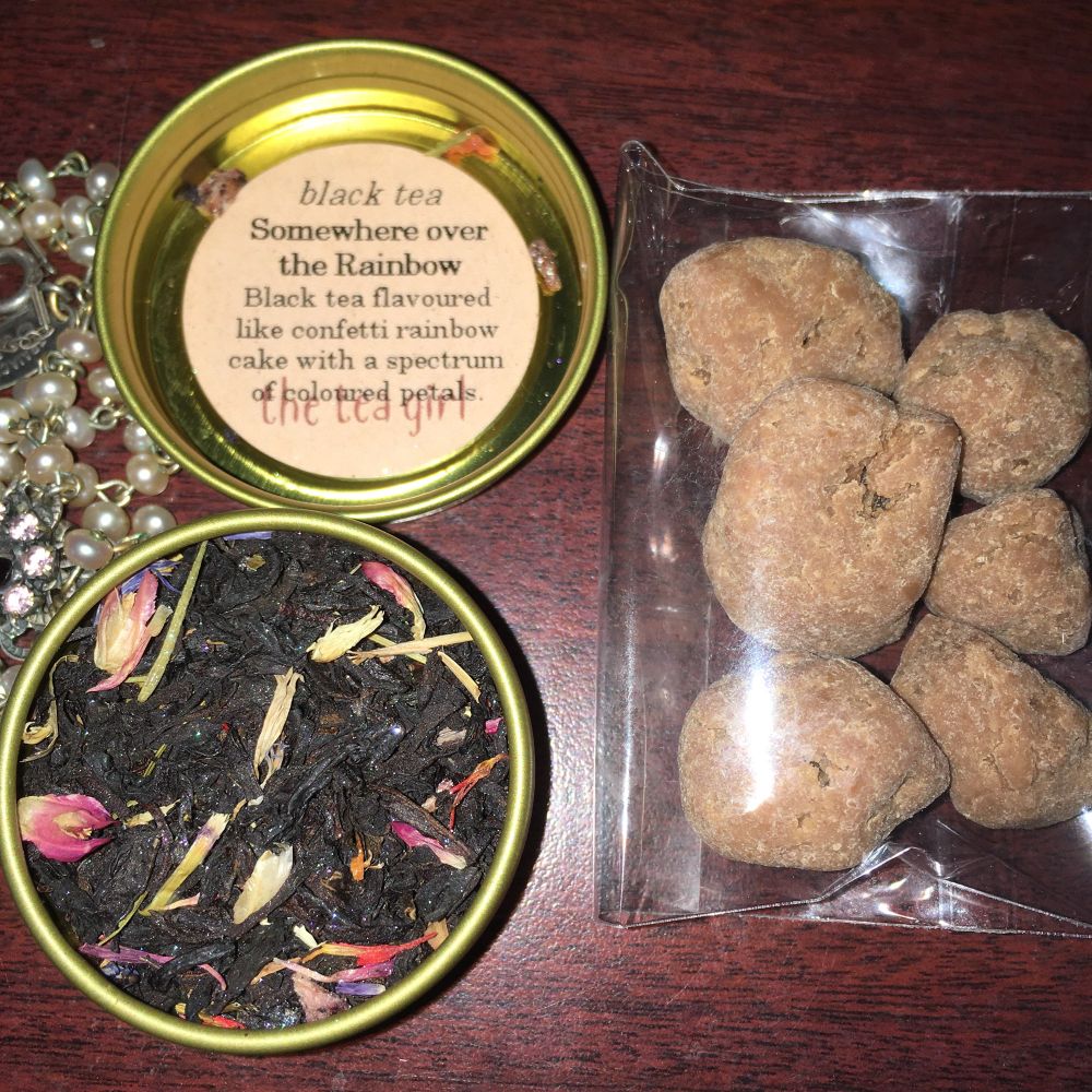 A container of glittery tea with rainbow petals scattered through it, next to a package of chocolate covered apricots