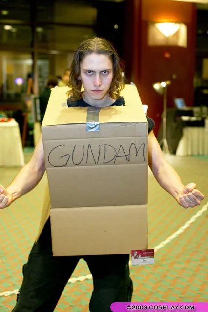 Photo de Paul M Palgeon, un cosplayeur portant un carton sur lui avec écrit "GUNDAM" dessus. Il prend une pose comme s'il chargeait son énergie