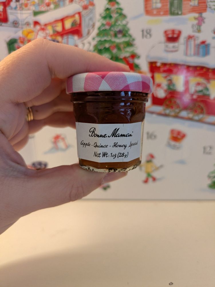 Small jar of jam, label reads "Bonne Maman Apple - Quince - Honey Spread Net Wt. 1 oz (28 g)" held in a hand