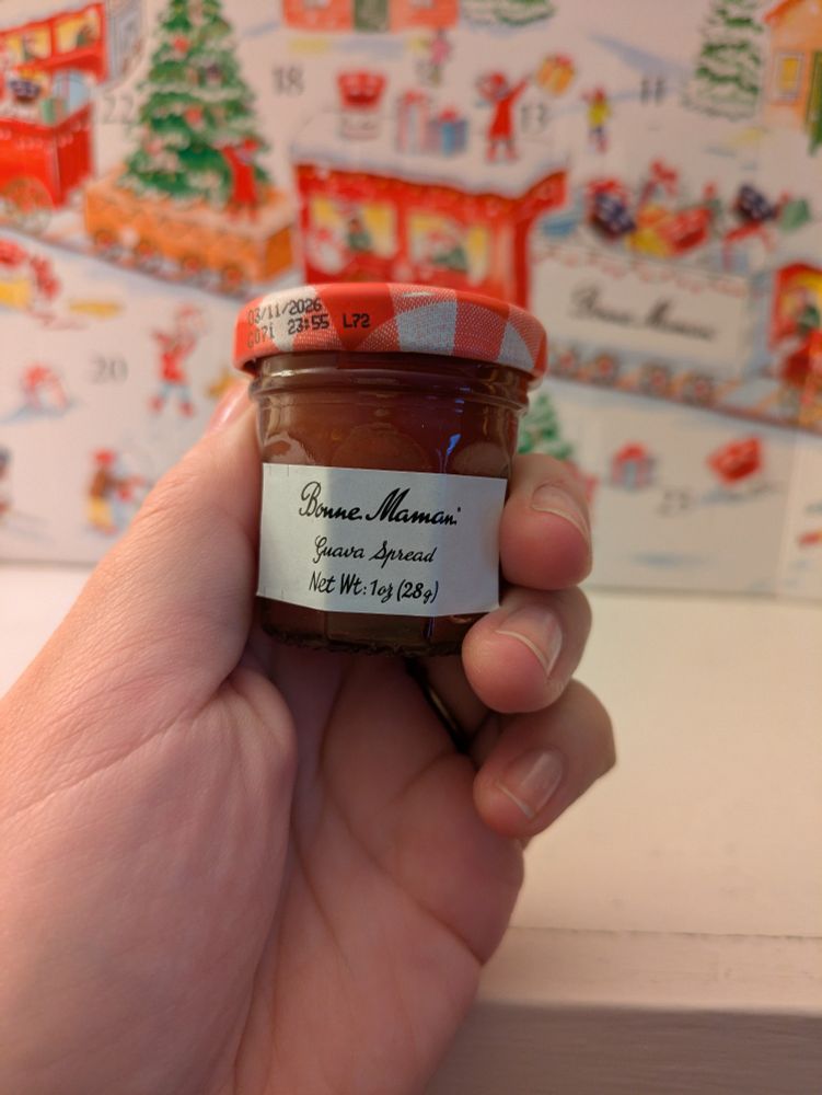 Small jar with jam and label that reads "Bonne Maman Guava Spread Net Wt. 1 oz (28g)" held in a hand