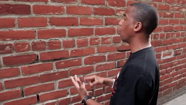 a man standing in front of a brick wall pointing