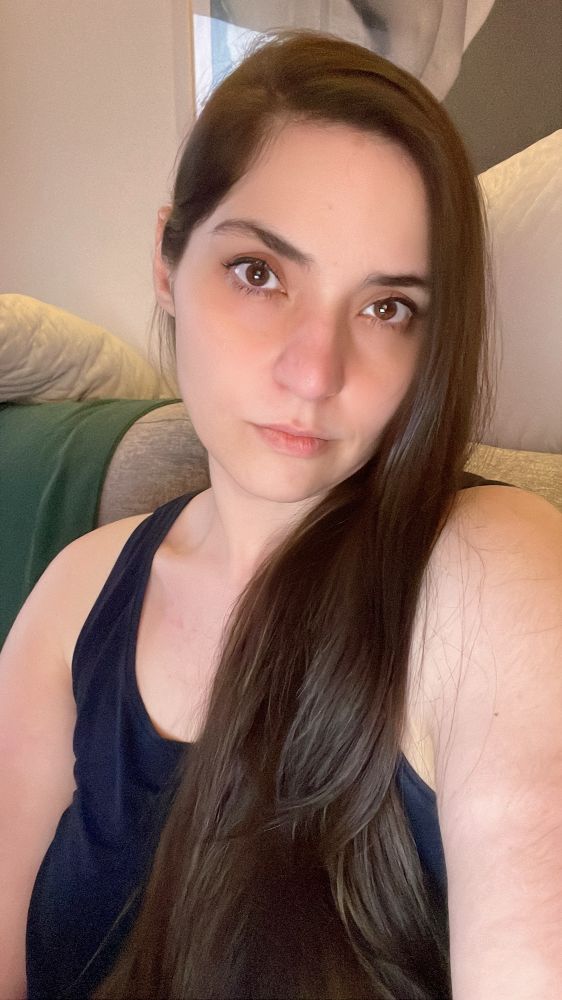 Eu, uma mulher branca de cabelo longo castanho e olhos castanhos. Uso uma regata azul