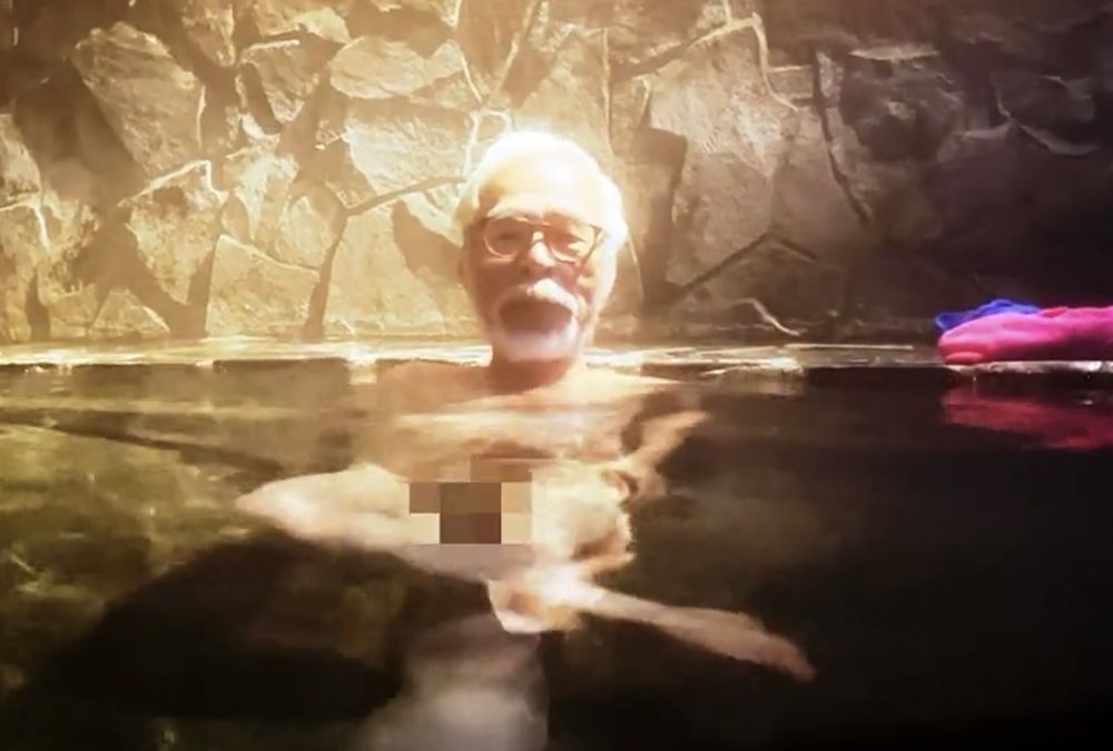 Miyazaki de pernas cruzadas numa espécie de ofurô. As genitais foram pixelizadas.