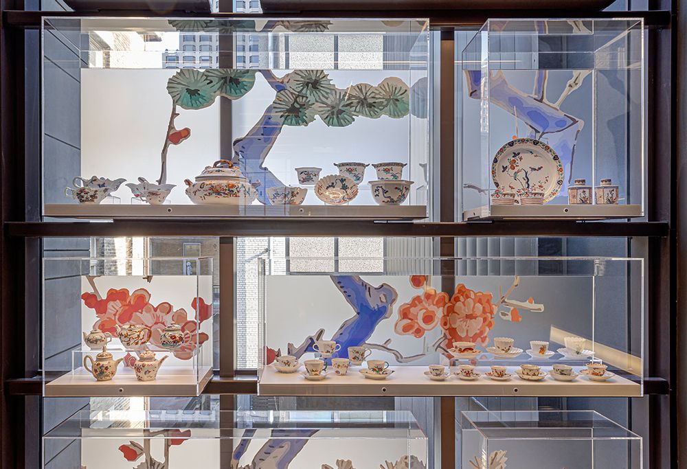 Vitrines on the staircase of the museum displaying various items from the Macdonald gift with backdrops of floral elements derived from the pieces themselves, in the characteristic blue, turquoise and orange of Arita porcelain