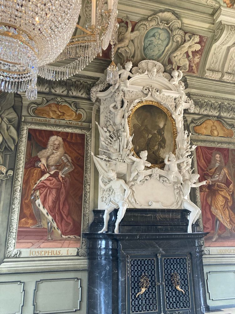 One of the marble stoves, with a black base and exuberant white putti, allegorical figures and military trophies above, flanked by (quite bad) portraits of past prince-bishops