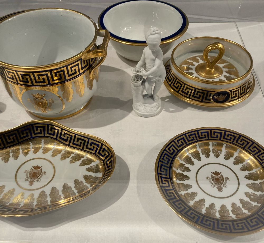 Neoclassical design with wide black (dark blue?) border with gilt Greek key pattern and acanthus leaves, arms on the central white panel. Small white biscuit porcelain  figure of a girl in the middle of the display of dishes