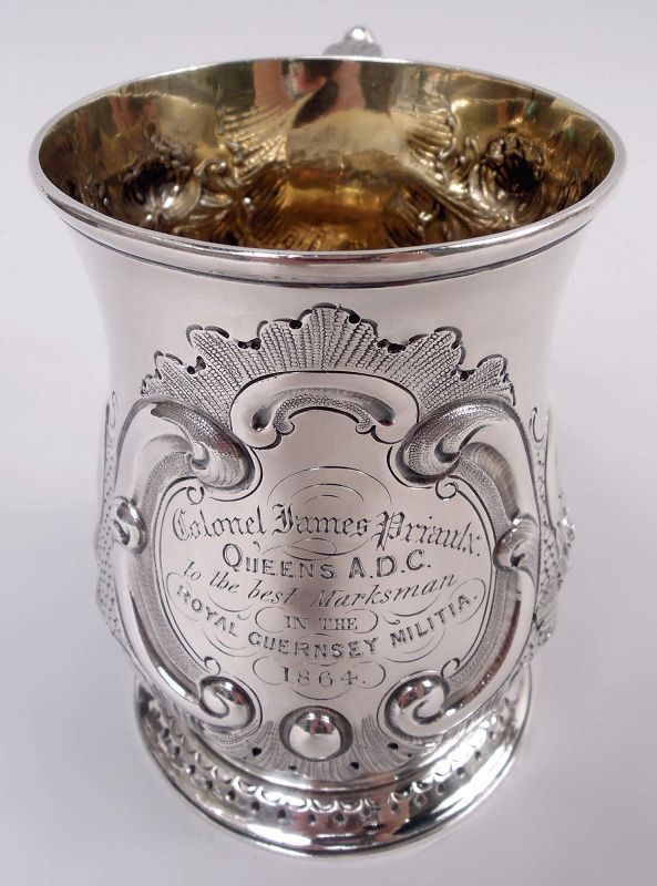 Baluster bowl with leaf-capped double-scroll handle and spread foot; gilt-washed interior. Chased and engraved scrolls and flowers. Scrolled frame in leaf and diaper surround with engraved presentation: 'Colonel James Priaulx / Queens A.D.C. / to the best Marksman / in the / Royal Guernsey Militia / 1864'