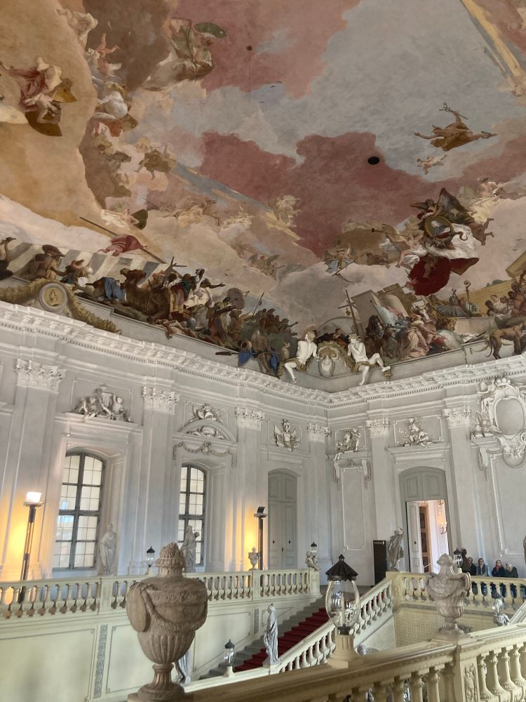 I can't do better than quote the elegant prose of Sir Michael Levey in Painting in Eighteenth-Century Venice (1959; 1994): 'No photographs unfortunately can give a proper conception of the ceiling as a whole, nor of the effect on the visitor slowly climbing the staircase as the vast fresco gradually expands before him. [...] Nothing less than the four Continents of the world are assebled to do homage to the reigning Prince-Bishop, Carl Philipp von Greiffenklau, whose ermine-draped portrait is upheld by putti while Fame trumpets his name to the ends of the earth. The extraordinary apotheosis of this petty and unimpressive person, one of a long line of Prince-Bishops whom the world has forgotten, is a triumph of sentiment over reason. So absurd, indeed, is it to suppose that the Continents would ever pay any attention whatsoever to Carl Philipp von Greiffenklau that the conception is almost imaginative. [...] Tiepolo's felicitous touch ... [keeps] the whole vast scheme fresh and lively and marvellously effortless. Never again could even Tiepolo express himself with such exuberance and enchanted virtuosity. Given the globe to create, his imagination expanded globally. Such an achievement could happen only once.'