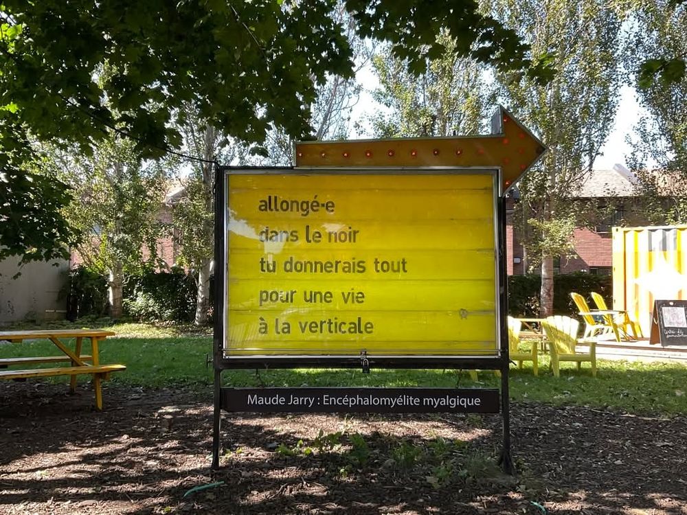 Dans un lieu calme ressemblant à un parc, un grand panneau d'affichage publicitaire. Il est surmonté d'une flèche géante.
Sur fond jaune, la phrase 
"allongé·e 
dans le noir
tu donnerais tout
pour une vie 
à la verticale"

Maude Jarry : Encéphalomyélite myalgique 