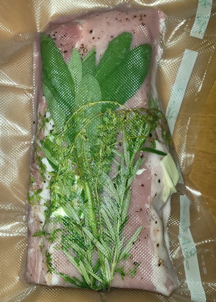 Pork loin in vaccum sealed plastic bag. A bunch of herbs, rosemary, sage,ans thyme, are on top.