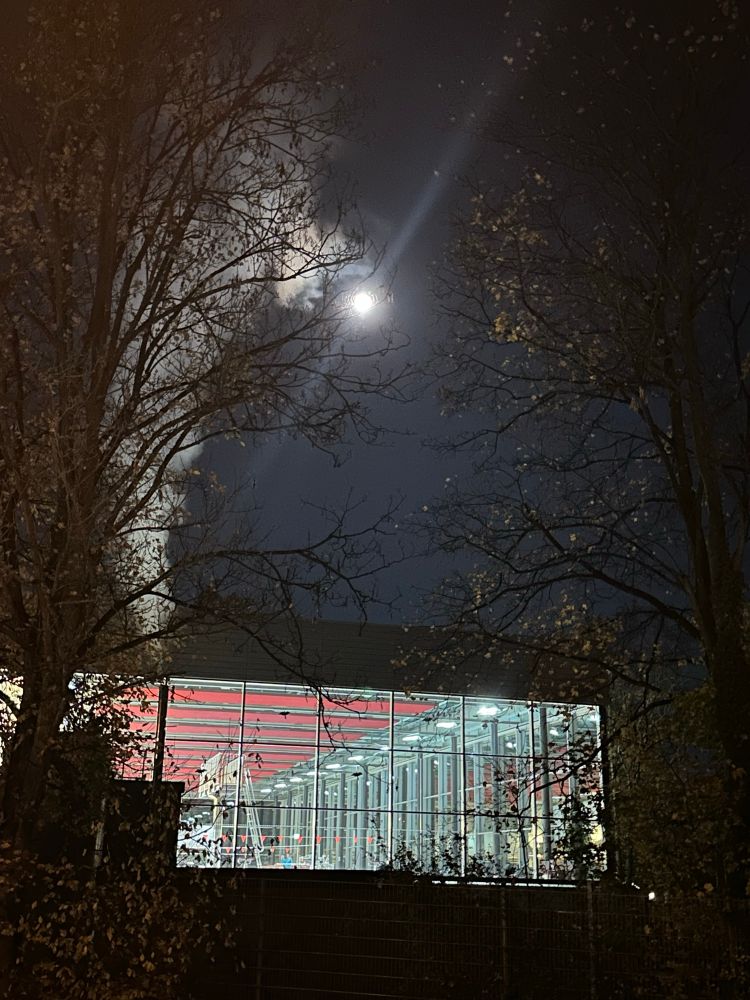Runder, strahlender, voller Mond über einem hell erleuchteten, rundum verglasten Hallenbad.
