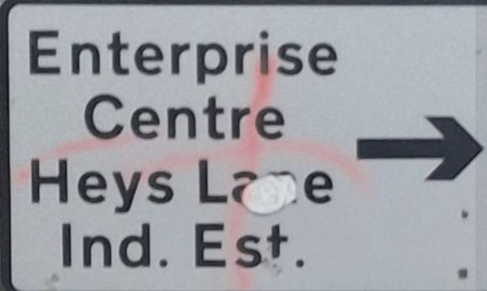 faint pink '+'  sprayed on a road sign 