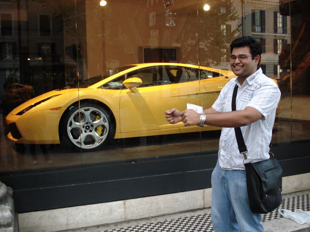 Me, 20 years ago, standing outside a car dealership where a prominent yellow Lamborghini sports car is on display. I'm posing as though I'm behind the wheel, but it's a sheepish grin as I know how stupid it looks.