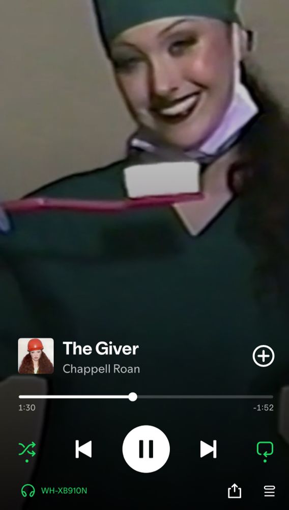 A screenshot from Spotify. Chappell Roan’s ‘The Giver’ is currently playing. The image shows her dressed in dentist scrubs with a novelty-sized toothbrush. The footage is intentionally low-quality and has a home cinema vibe 
