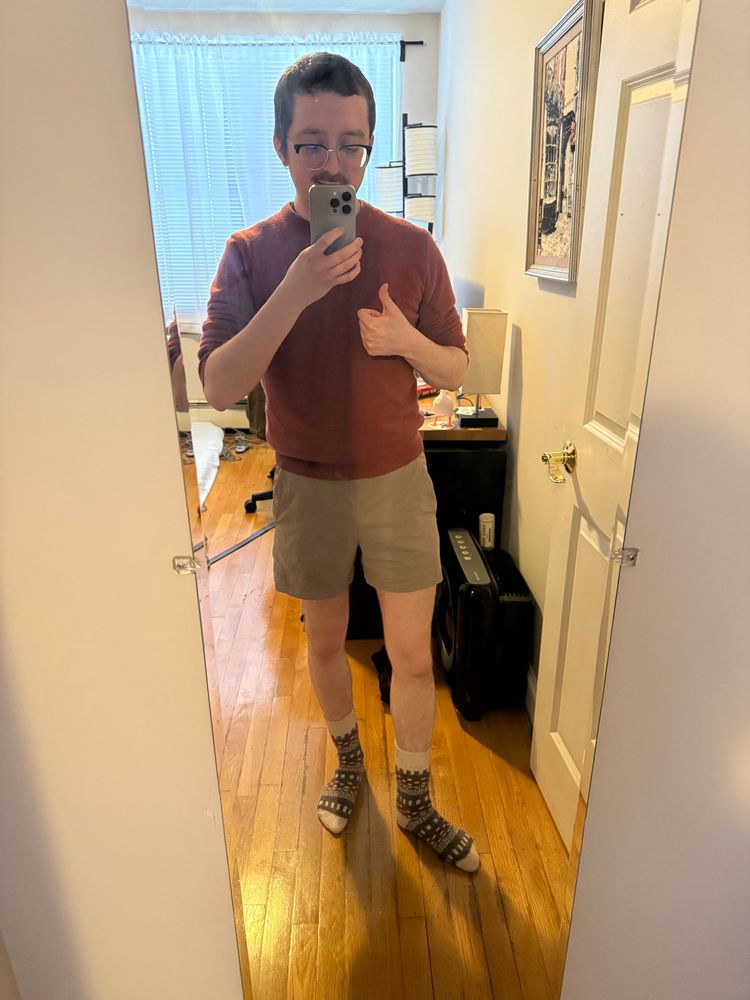 myself standing in front of a mirror with shorts and a red sweater on giving a thumbs up 