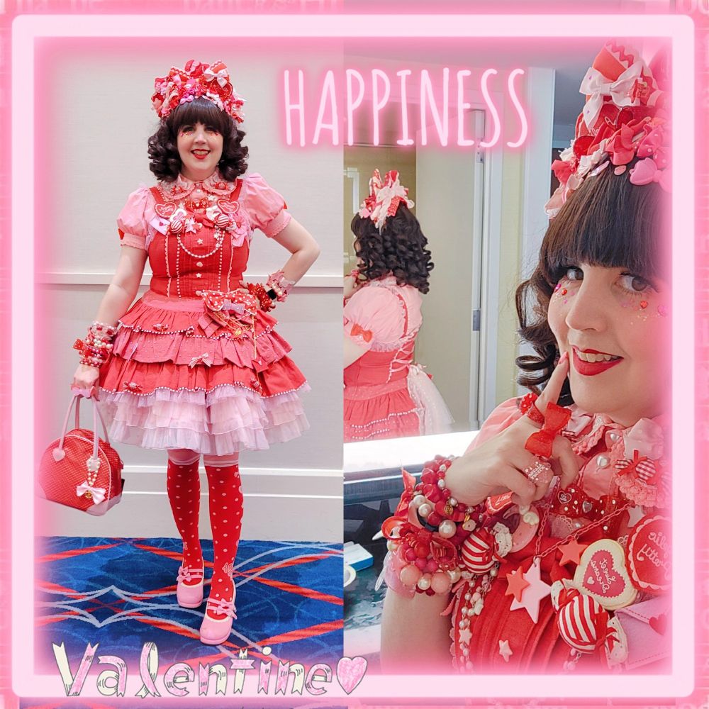 A woman wearing a red tiered angelic pretty dress with pink ruffles at the hem and a pink blouse under it. She is wearing red polka dot socks and pink shoes. On her head is a curly brown wig and lots of red and pink hair bows. She's holding a red polka dot purse and is covered in heart and candy shaped pins.