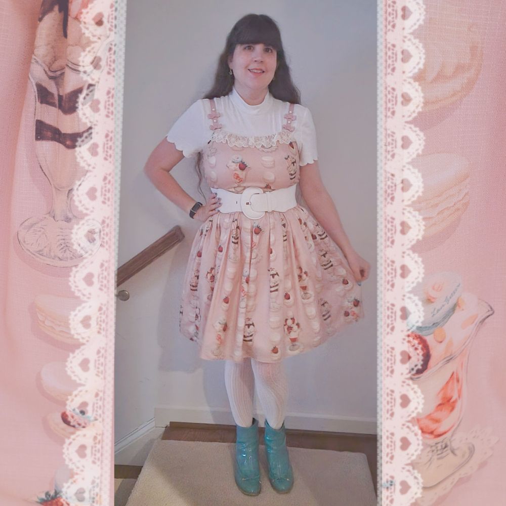 A woman with dark hair wearing a pink dress printed with macarons, a white belt, white lace tights and a white shirt with teal rainboots