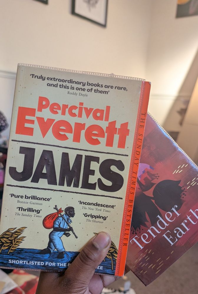 Picture of a hand holding two books, Percival Everett's James and Sita Brahmachari's Tender Earth 
