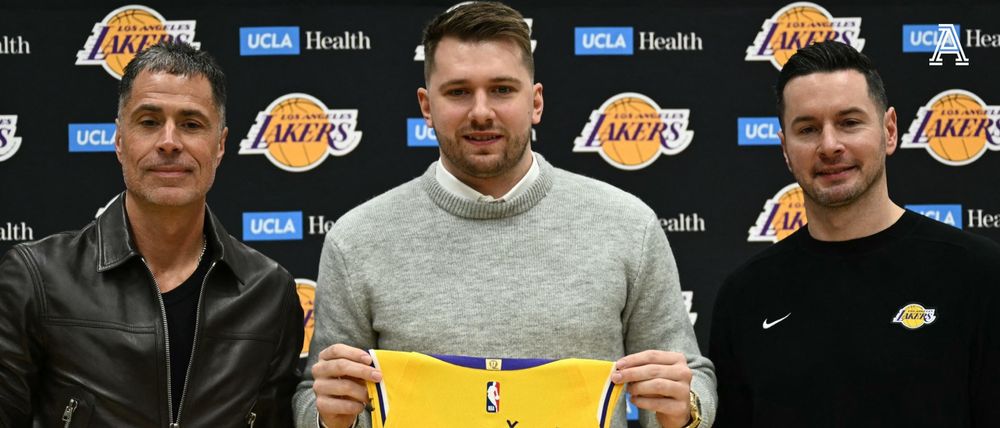 crop of photo of luka being presented as a laker, with rob pelinka (left) in a 'white guy trying very hard to be cool' leather jacked, luka (center) cleaned up with a sweater over a collared shirt, and jj redick (right) in a team issued black sweatshirt with the forced smile of a man whose wife just left him