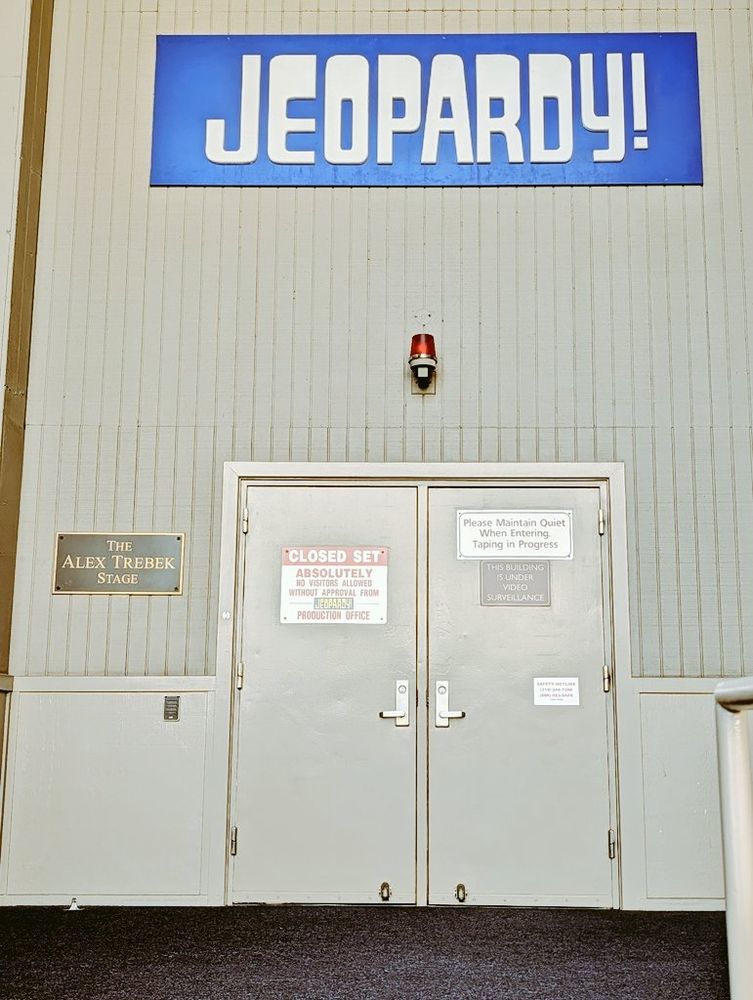 A photo of the blue Jeopardy sign and doors into the studio. On the left is a plaque that says Alex Trebek stage