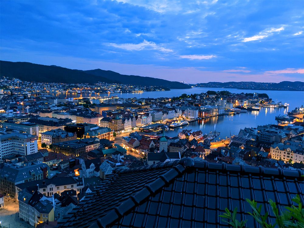 The classic view of Bergen from partway down Fløyen, but in blue twilight. Some tinges of the pink sunset remain at the horizon and the city is full of warm yellow artificial light.