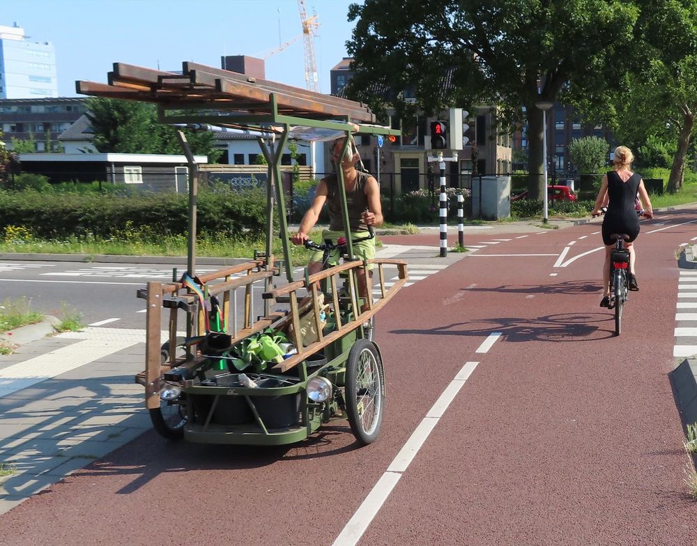 A man rides an adapted bike with several sets of ladders and other tools on it 