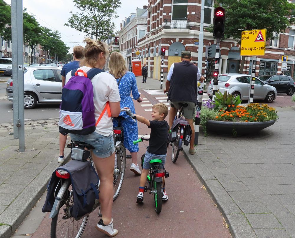 A cycle track in the Netherlands at a red light, with 5 people waiting, including a mum and her young son. 