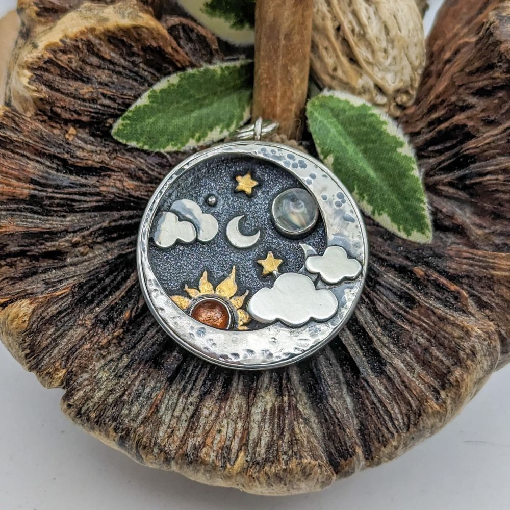 Shadowbox pocket watch. Sterling silver pendant deep to create layers in the pendant with a textured and oxidized background silver moon, and clouds, keum boo guilded stars and sun with a sunstone center. A moonstone moon, textured crescent moon foreground and silver clouds. 